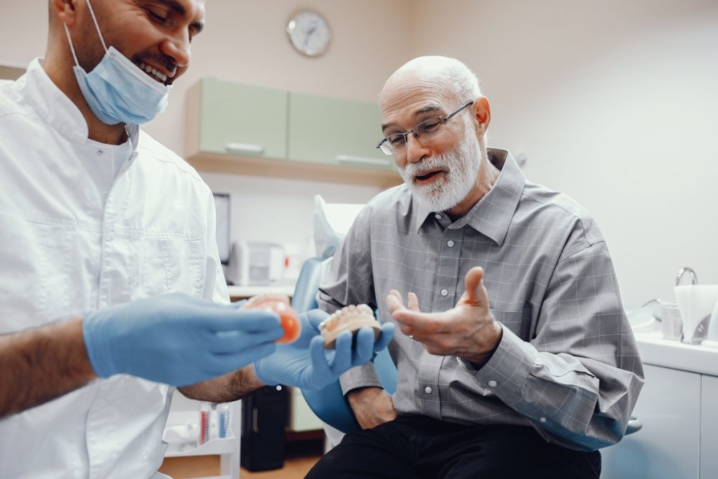 Dentist smiling with senior patient while showing custom dentures at Dental Arts Toronto clinic